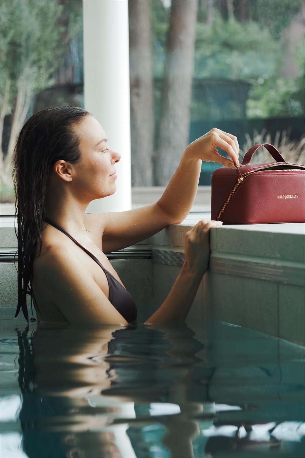 Model in pool zipping up Wild Atelier Special Edition Leather Travel Case
