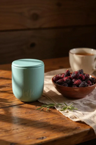 Mulberry and Rosemary Limited Edition Candle sat on rustic table top next to bowl of blackberries and cup of tea