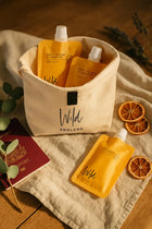 Wild England natural hand and body wash and lotion, shampoo sweet orange and cardamom pouches 50ml tucked into a small canvas bag, next to a passport and dried orange slices