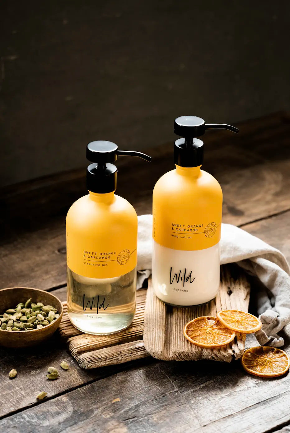 Wild England natural two bottle starter set sweet orange and cardamom hand and body wash and lotion 475ml on rustic wooden surface next to dried orange slices