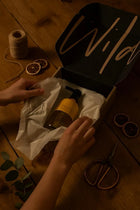 Wild England single bottle gift box with model revealing sweet orange and cardamom 475ml natural hand and body wash bottle inside the packaging, next to dried oranges, string and scissors on a rustic wooden surface